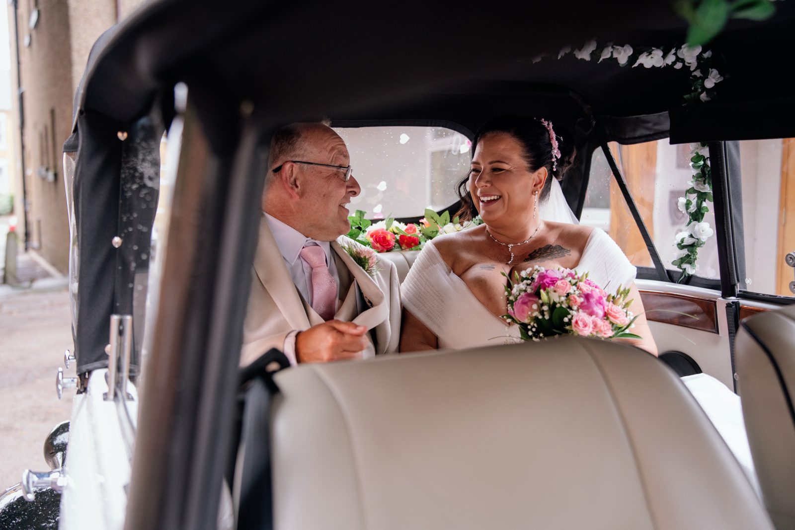 Bride and father sharing a laugh inside the wedding car